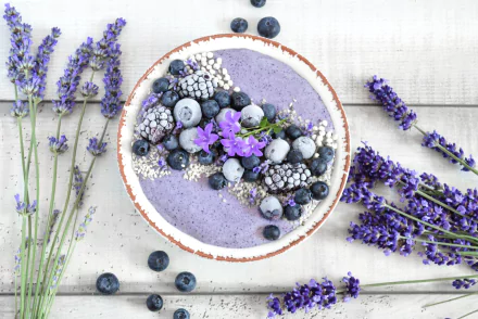 HD desktop wallpaper featuring a blueberry smoothie bowl topped with fresh berries, edible flowers, and surrounded by sprigs of lavender, blending food and floral still life.