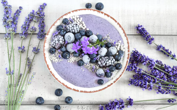 HD desktop wallpaper featuring a blueberry smoothie bowl topped with fresh berries, edible flowers, and surrounded by sprigs of lavender, blending food and floral still life.