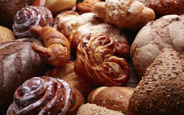 HD desktop wallpaper featuring an assortment of freshly baked viennoiserie, including croissants and various breads, showcasing rich textures and golden crusts.