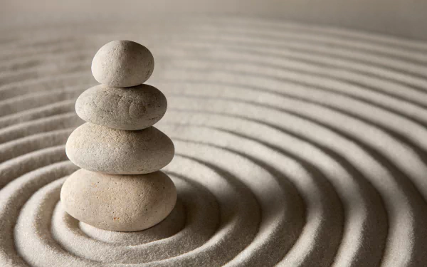 Close-up 5K Ultra HD PC desktop wallpaper of stacked zen stones on raked sand rings, natural textures and soft shadows, calming nature background.