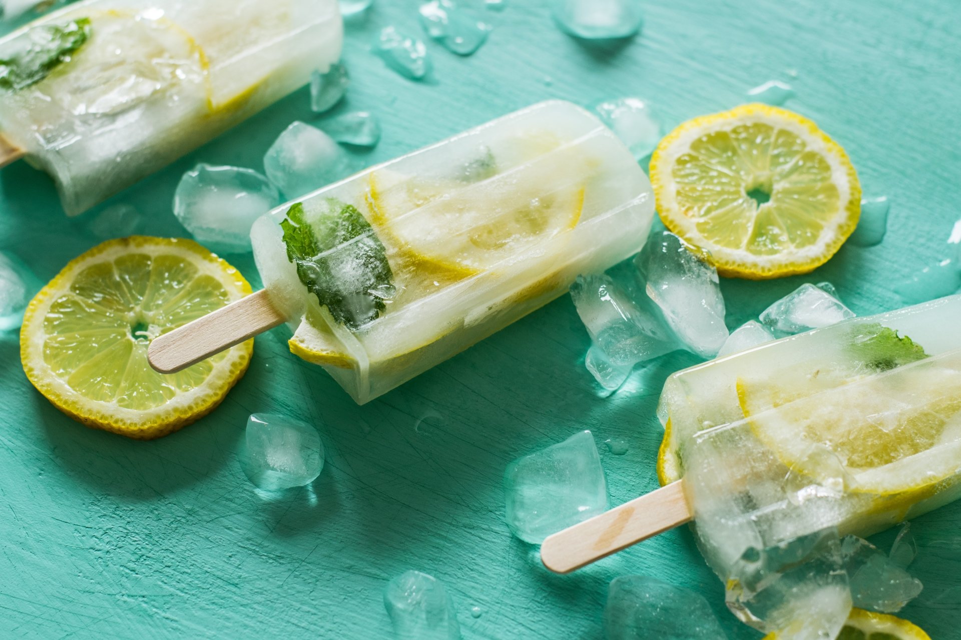 Close-up still life of lemon ice cream popsicles with ice cubes and lemon slices on a turquoise surface, captured in 4K Ultra HD for a vibrant PC desktop wallpaper.