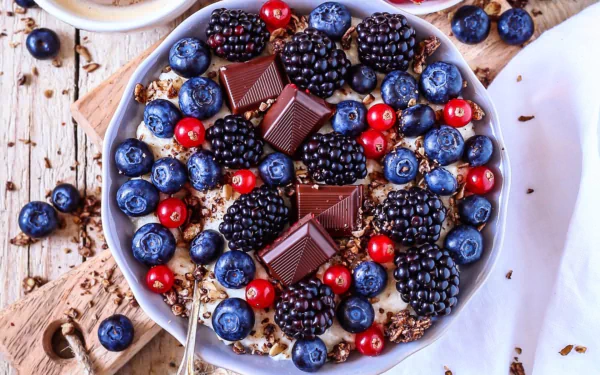 HD desktop wallpaper: still-life breakfast bowl of blackberries, blueberries and red currants with granola, chocolate squares and coffee on a rustic board.