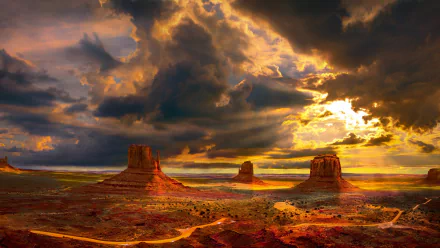 HD PC desktop wallpaper featuring Monument Valley's desert landscape under dramatic, cloudy skies during a vibrant sunset.