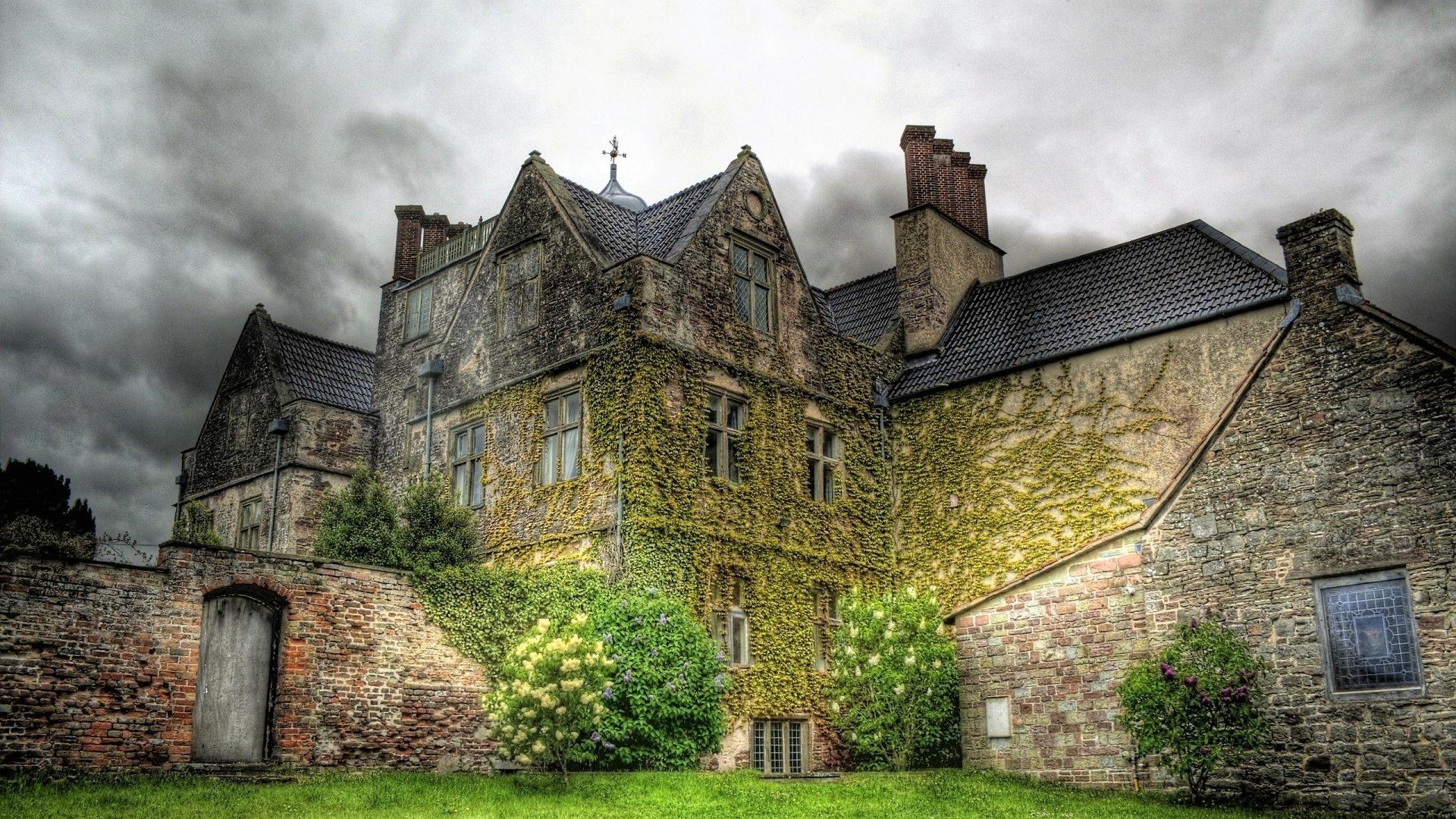Ivy-clad Edinburgh Castle in Scotland, dramatic cloudy sky over a man-made historic stone structure and green lawn — 2K Quad HD PC desktop wallpaper/background.