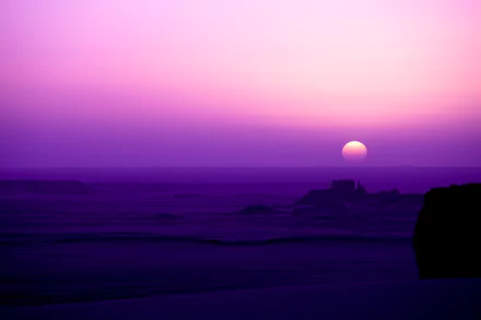 A stunning HD desktop wallpaper of the Sahara Desert at sunrise, featuring purple skies and sunlit sand dunes in Tassili N'Ajjer, Algeria, Africa.