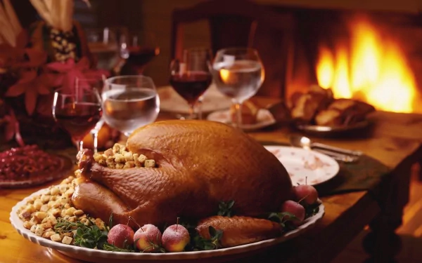 A beautifully set Thanksgiving table features a golden-brown turkey surrounded by garnishes, with elegant glassware and a warm fireplace in the background, creating a festive atmosphere.