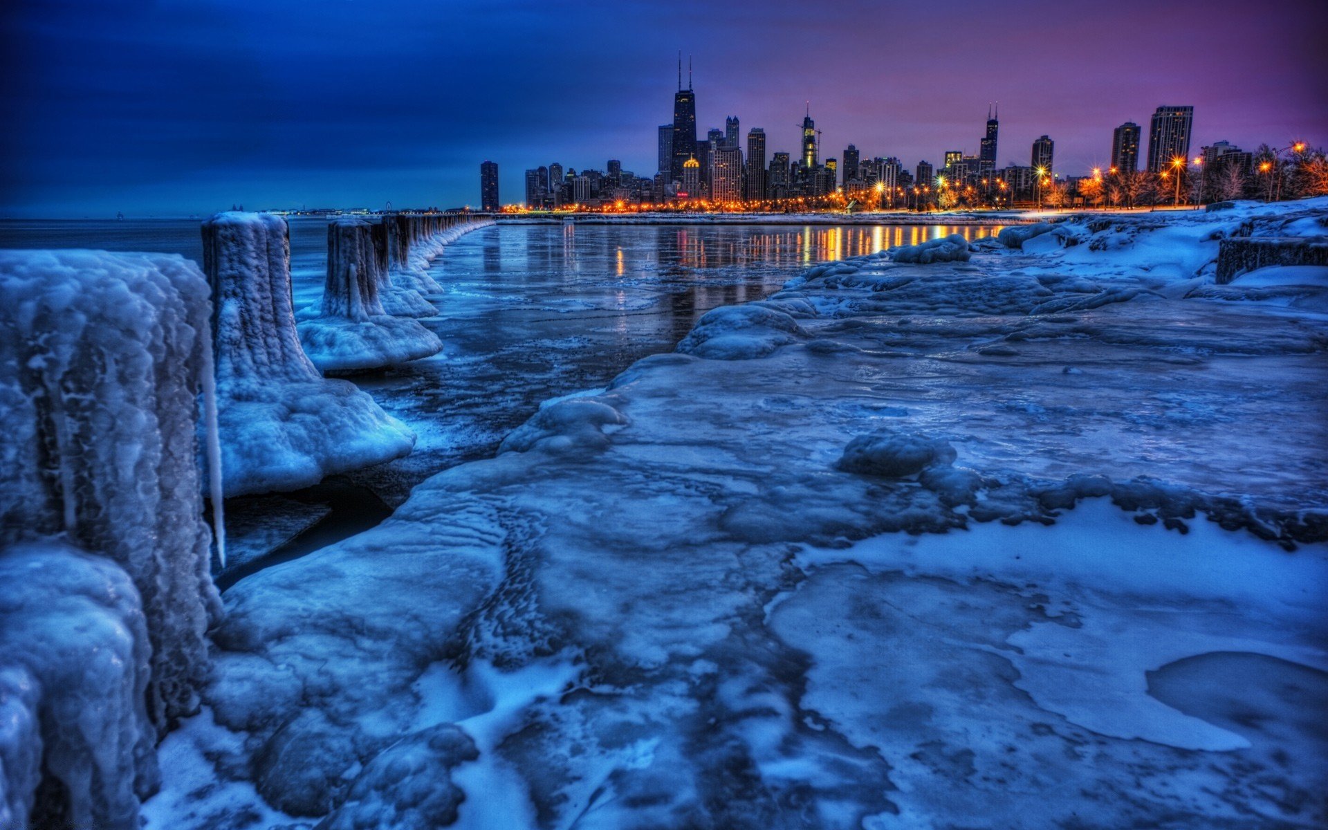 A stunning winter scene featuring icy shores and a vibrant city skyline illuminated by twilight. This high-definition nature wallpaper captures the serene beauty of winter.