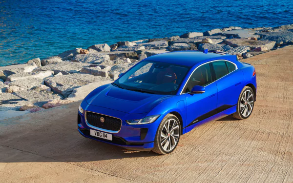 Blue Jaguar I-Pace electric vehicle parked near rocky shoreline, captured in stunning 4K Ultra HD quality as a desktop wallpaper and background image.