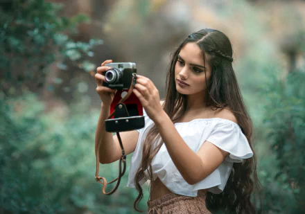 A brunette woman with long hair holds a camera, capturing a photo with a shallow depth of field in a lush outdoor setting, presented as an HD PC desktop wallpaper.
