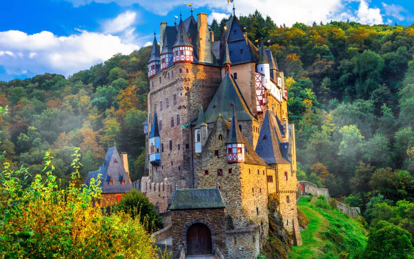 4K Ultra HD wallpaper featuring Eltz Castle, a man-made historic castle surrounded by vibrant fall foliage under a bright blue sky.