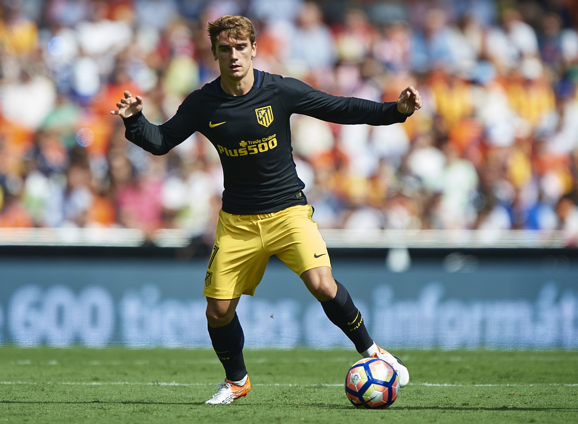 French soccer player in a dark training top and yellow shorts controls the ball on a packed stadium pitch — high-resolution 4K sports desktop wallpaper.