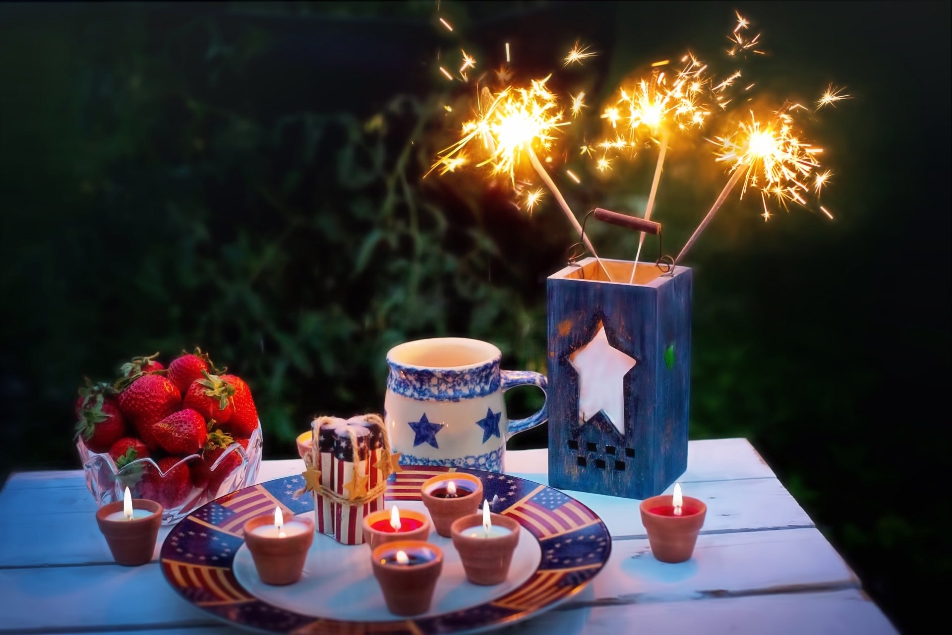 A festive 4th of July still life with sparklers, strawberries, star-decorated mugs, and candles, set as an HD PC desktop wallpaper celebrating Independence Day.