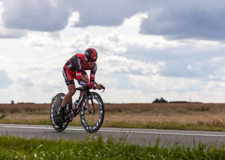 A cyclist in red and black gear rides a racing bicycle on an open road under a cloudy sky, capturing the spirit of cycling and sports in this HD desktop wallpaper.