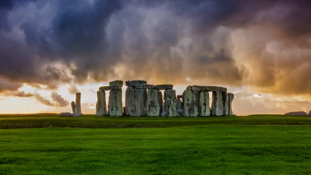 Stonehenge standing on lush green grass under a dramatic cloudy sky, captured in vivid 4K Ultra HD as a striking man-made stone monument background.