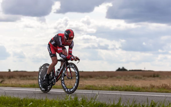 A cyclist in red and black gear rides a racing bicycle on an open road under a cloudy sky, capturing the spirit of cycling and sports in this HD desktop wallpaper.