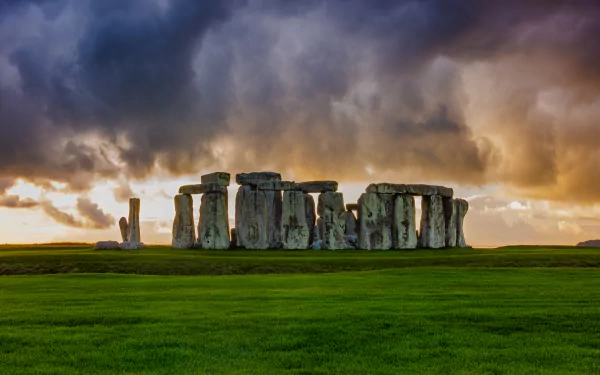 Stonehenge standing on lush green grass under a dramatic cloudy sky, captured in vivid 4K Ultra HD as a striking man-made stone monument background.