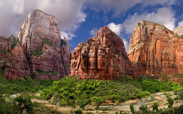 HD PC desktop wallpaper of Zion National Park canyon: towering red sandstone cliffs and mountains rising above green trees and a winding valley under a blue sky.
