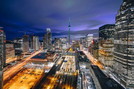 Nighttime Toronto skyline with CN Tower rising among glass skyscrapers and glowing city streets — HD PC desktop wallpaper of a man-made urban landscape in Canada.