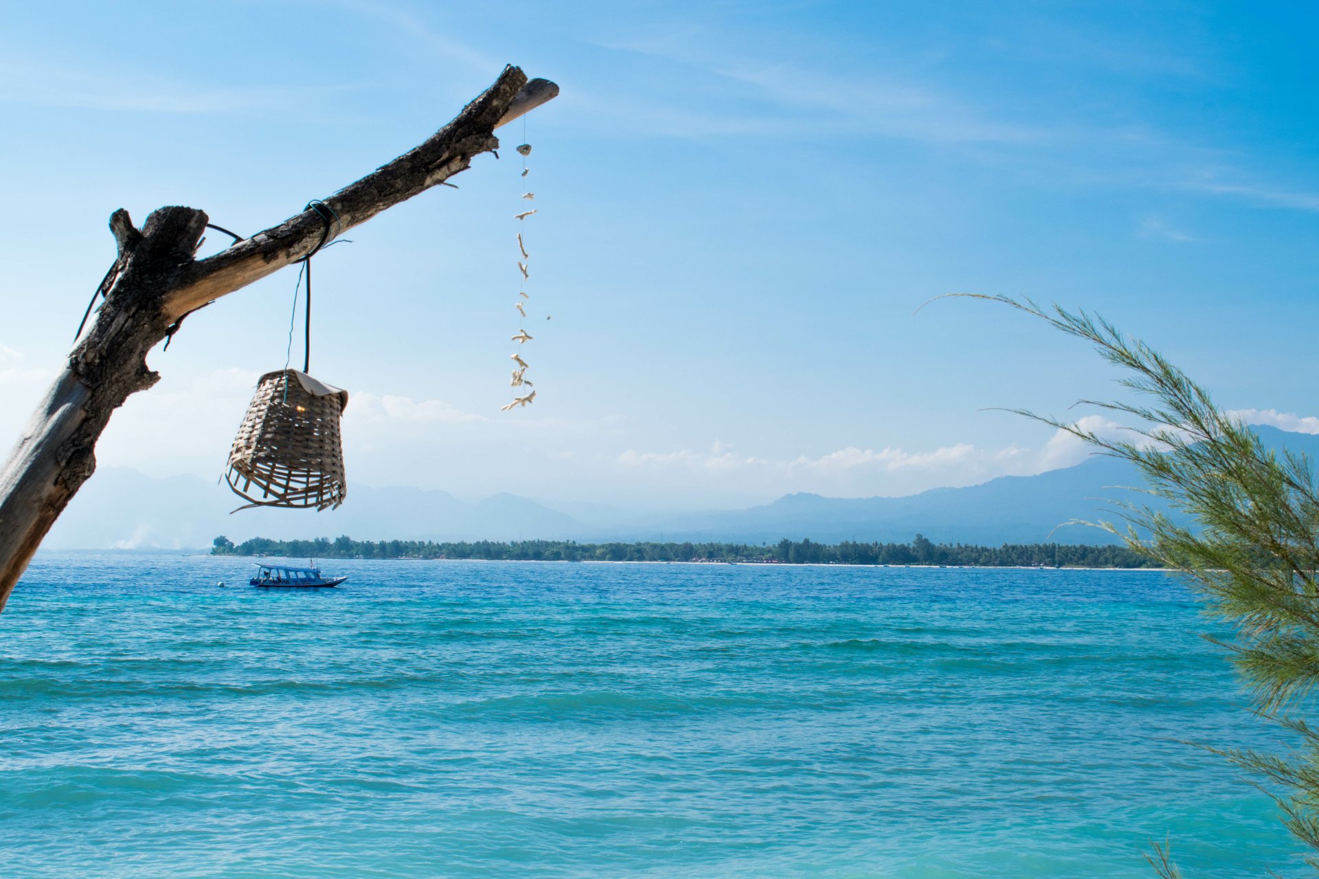 5K Ultra HD desktop wallpaper: fishing basket dangling from driftwood above turquoise sea off Gili Meno, boat on the horizon — vibrant nature photography.