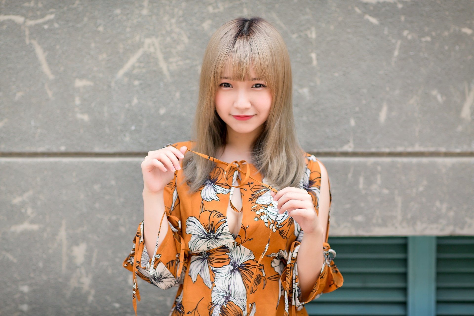 HD PC desktop wallpaper featuring a smiling Asian woman with blonde hair wearing an orange floral dress against a gray textured background.