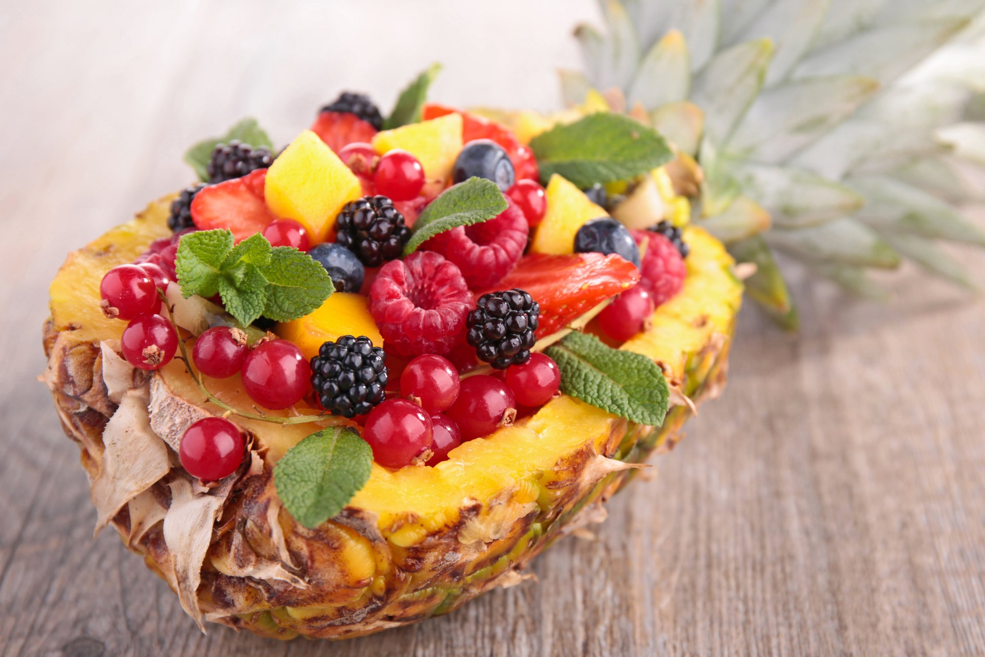 2K Quad HD PC desktop wallpaper of a halved pineapple filled with strawberries, blackberries, red currants and mango, garnished with mint — vibrant fruit and berry food image.