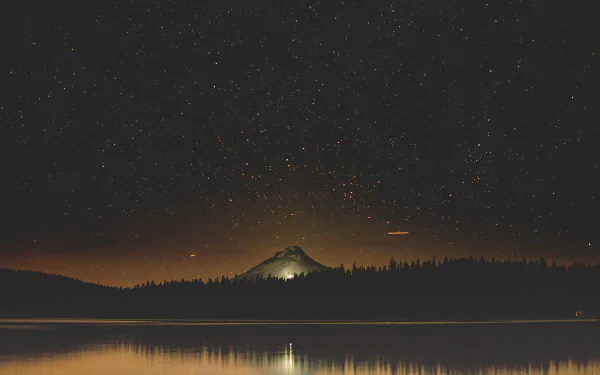 8K Ultra HD wallpaper showing a tranquil lake under a starry night sky with a softly lit hill and natural silhouettes in the background.