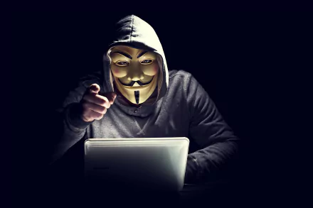 4K Ultra HD desktop wallpaper showing an anonymous figure in a hoodie and Guy Fawkes mask working on a laptop, symbolizing technology and online anonymity.