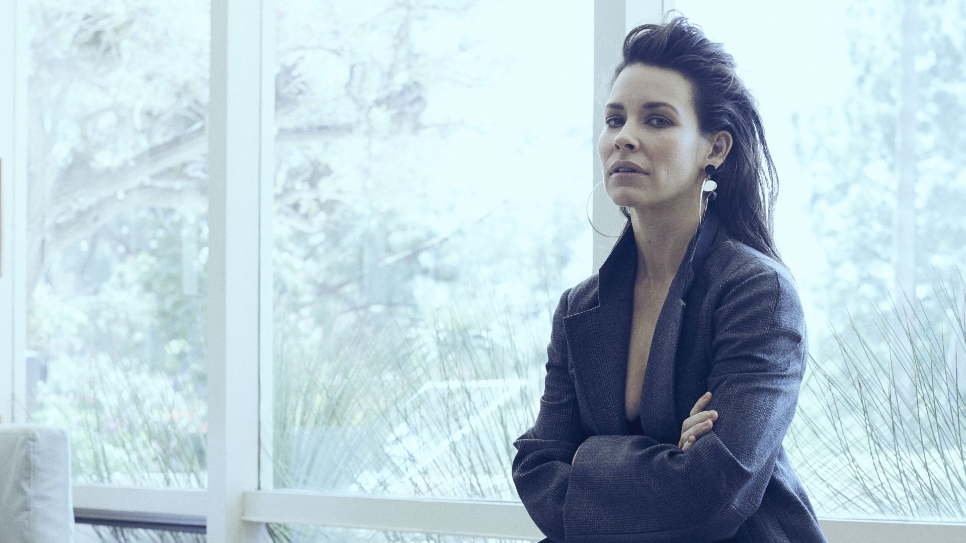 4K Ultra HD PC desktop wallpaper: poised female celebrity in a dark blazer stands by a bright window with arms crossed, gazing contemplatively.