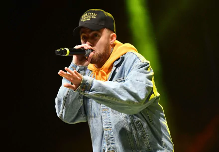 HD wallpaper of a performer in a denim jacket and cap singing into a microphone on stage.