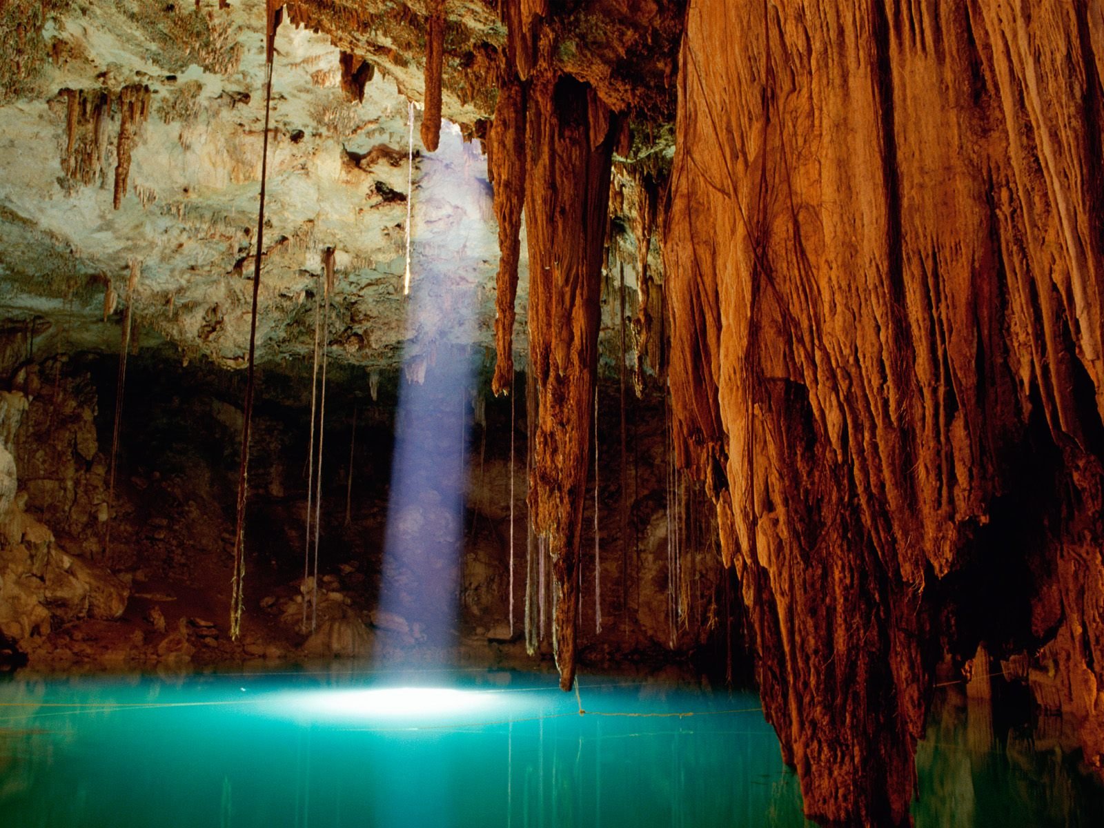 A stunning HD wallpaper featuring a serene cave scene illuminated by a beam of light, with natural rock formations and a tranquil pool of water, showcasing the beauty of nature.