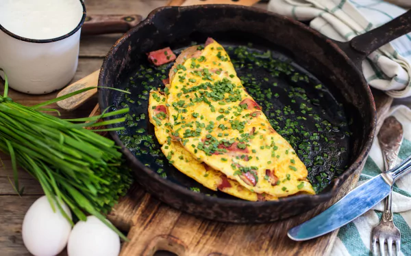 5K Ultra HD PC desktop wallpaper still life: folded ham-and-chive omelette in a cast-iron skillet with eggs, chives and a cup of milk on a wooden board.