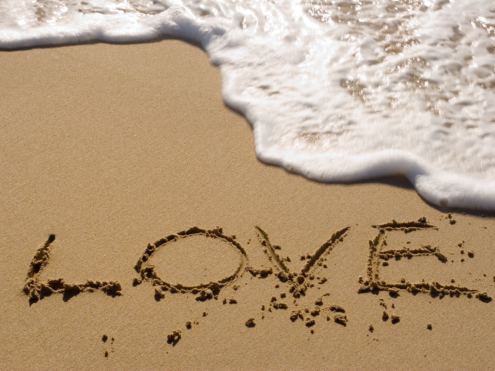 An artistic HD desktop wallpaper featuring the word LOVE written in the sand, gently kissed by waves, creating a serene and romantic atmosphere.