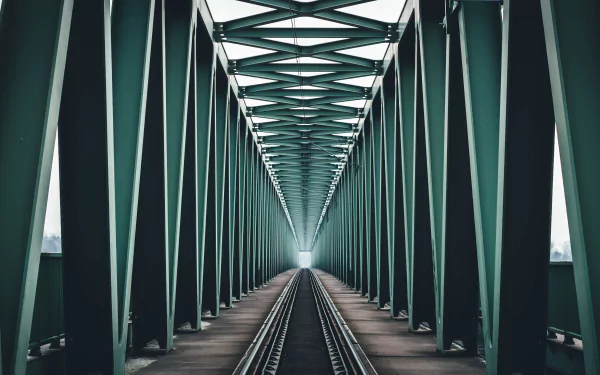 Railroad tracks receding through a green steel truss bridge with a strong vanishing point — 5K Ultra HD PC desktop wallpaper/background, man-made structure.