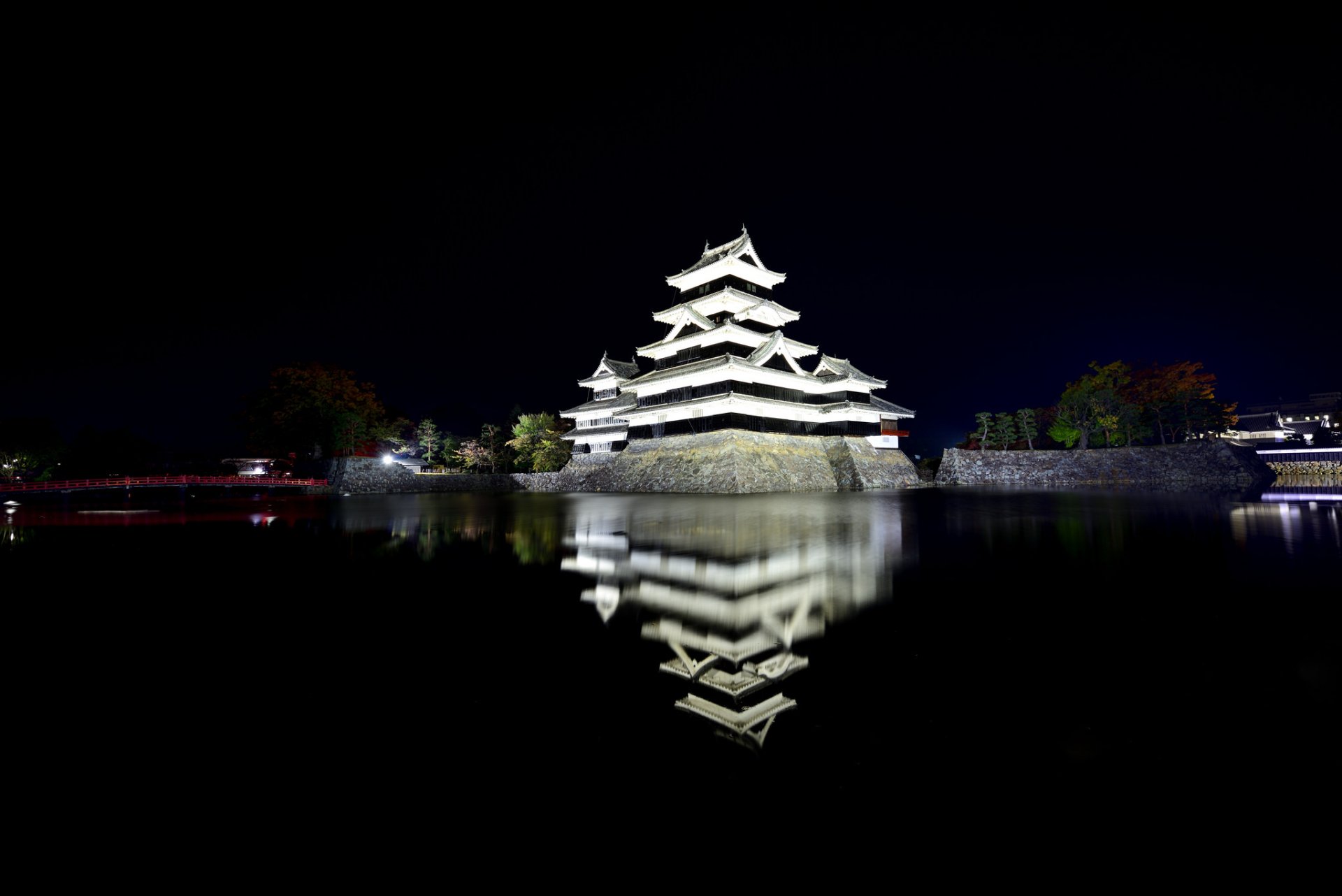Night view of Matsumoto Castle in Japan, showcasing its traditional architecture reflected in the surrounding water against a dark sky, captured in HD for desktop wallpaper.
