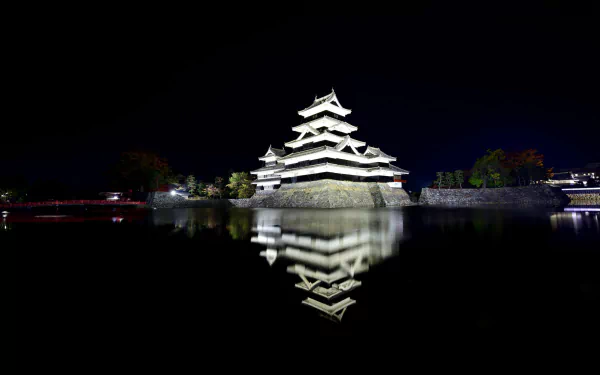 Night view of Matsumoto Castle in Japan, showcasing its traditional architecture reflected in the surrounding water against a dark sky, captured in HD for desktop wallpaper.