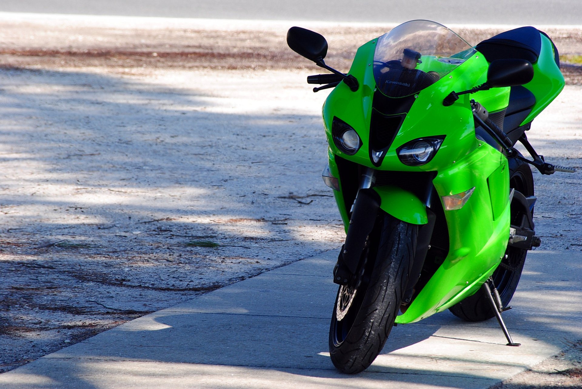 HD PC desktop wallpaper featuring a vibrant green Kawasaki motorcycle parked on a paved surface with natural sunlight highlighting its sleek design.