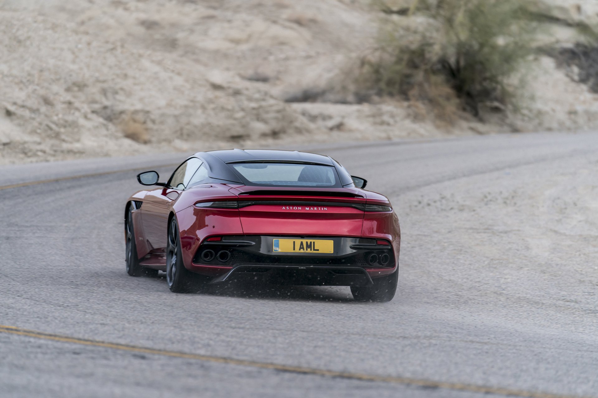 HD desktop wallpaper featuring a red Aston Martin DBS Superleggera supercar driving on a winding desert road.