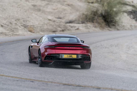 HD desktop wallpaper featuring a red Aston Martin DBS Superleggera supercar driving on a winding desert road.