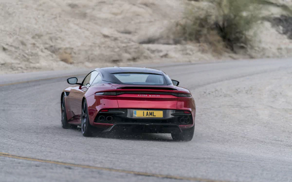 HD desktop wallpaper featuring a red Aston Martin DBS Superleggera supercar driving on a winding desert road.