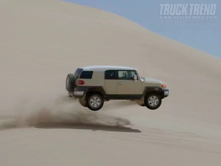 A Toyota FJ Cruiser airborne over sand dunes, captured in an HD desktop wallpaper showcasing rugged off-road adventure.