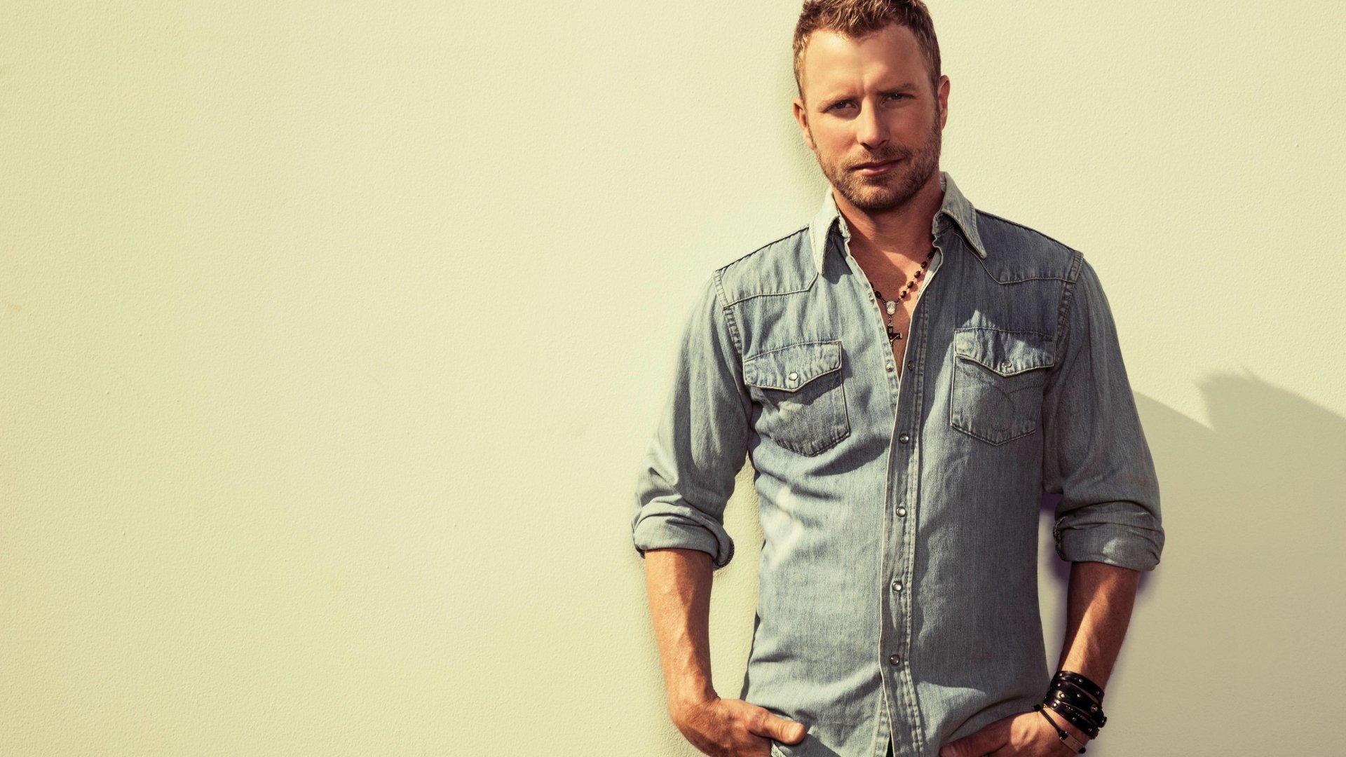 HD desktop wallpaper featuring a man in a denim shirt posing confidently against a neutral background.