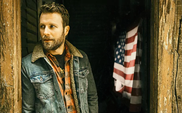 HD desktop wallpaper featuring Dierks Bentley in a denim jacket, leaning against a rustic doorway with an American flag in the background.
