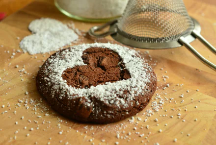 Heart-shaped chocolate cookie dusted with powdered sugar on a wooden board, with a sieve and flour nearby — 4K Ultra HD PC desktop wallpaper and background.
