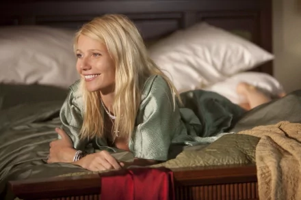 Gwyneth Paltrow relaxes on a bed, smiling warmly. This high-definition image serves as an elegant desktop wallpaper, capturing a moment of comfort and charm.