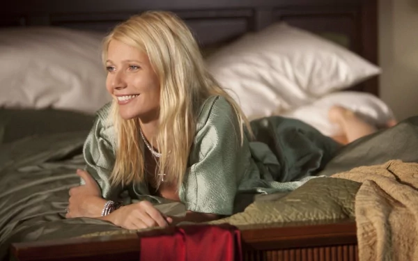 Gwyneth Paltrow relaxes on a bed, smiling warmly. This high-definition image serves as an elegant desktop wallpaper, capturing a moment of comfort and charm.