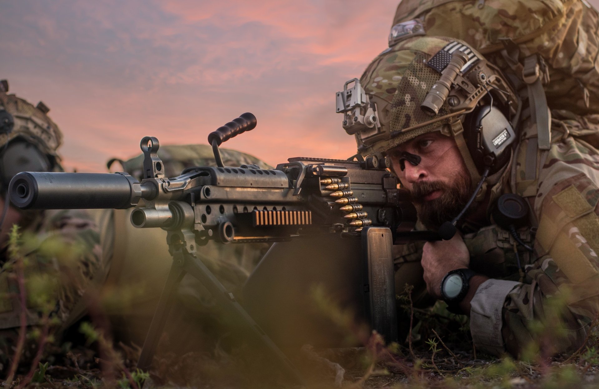 Camouflaged soldier prone operating a belt-fed machine gun at sunset — military scene, 5K Ultra HD PC desktop wallpaper/background