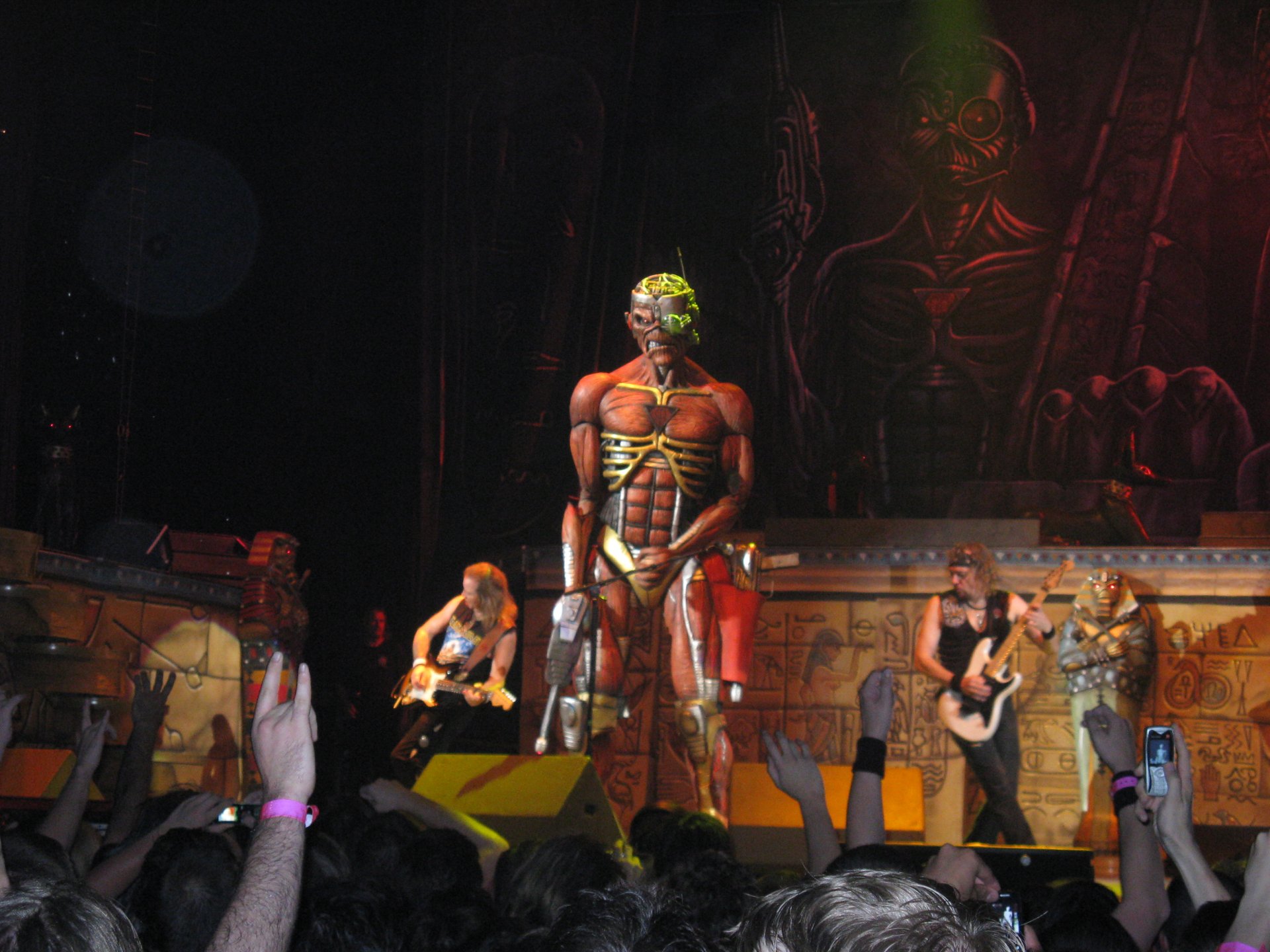 A dynamic Iron Maiden concert scene featuring a large, iconic Eddie statue on stage, with band members performing and an enthusiastic crowd in the foreground. A striking HD desktop wallpaper.