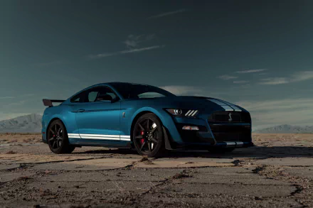 A sleek blue Ford Mustang Shelby GT500 muscle car with white racing stripes parked on cracked desert ground under a dramatic sky, captured in 8K Ultra HD.