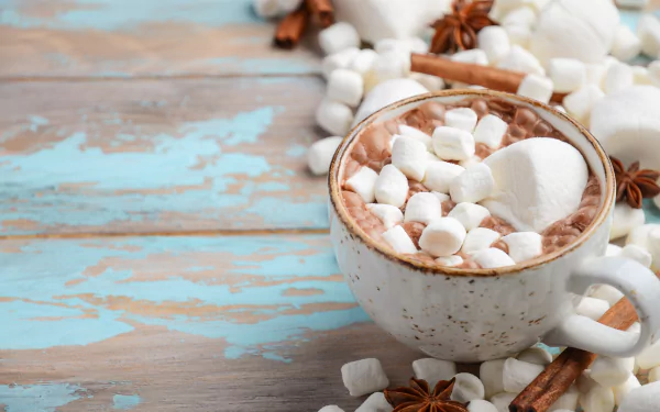 A 4K Ultra HD desktop wallpaper showing a rustic cup of hot chocolate topped with marshmallows, surrounded by scattered marshmallows and cinnamon sticks on a wooden surface.