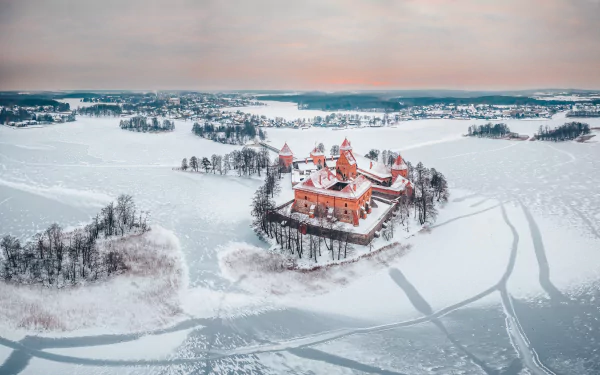 A winter landscape of Lithuania’s Trakai Island Castle surrounded by frozen lake and snow-covered land under a calm horizon.